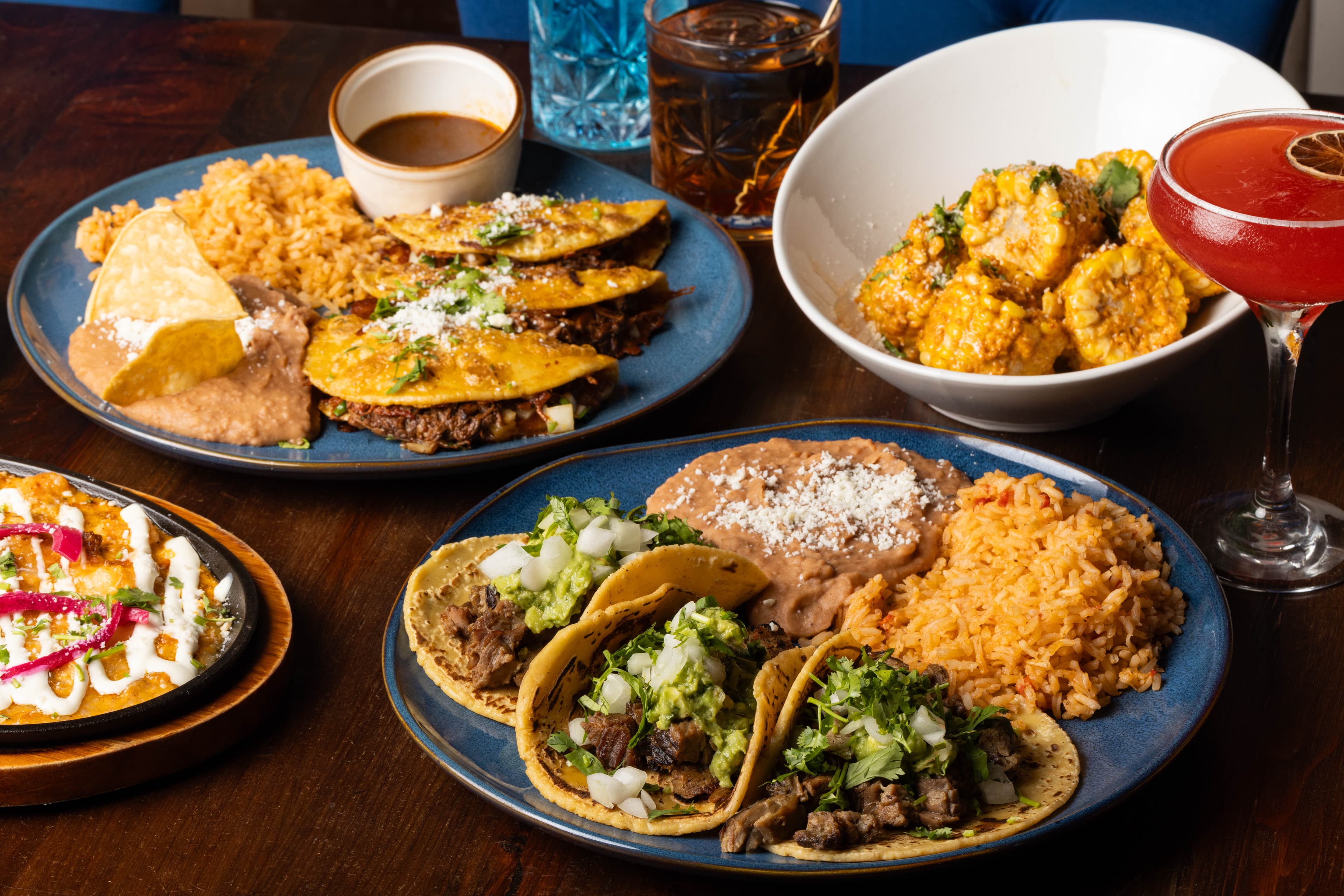 A spread of El Sueño tacos, birria, elote, and craft cocktails
